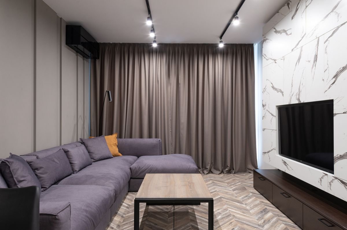 Gray L-shaped sofa beside curtains and a TV in a living room.