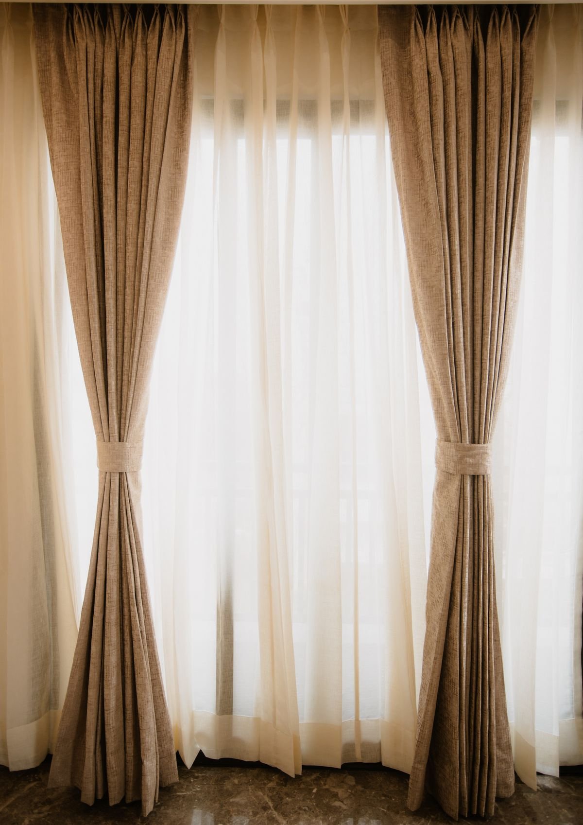 Beige drapes tied back beside sheer white curtains.