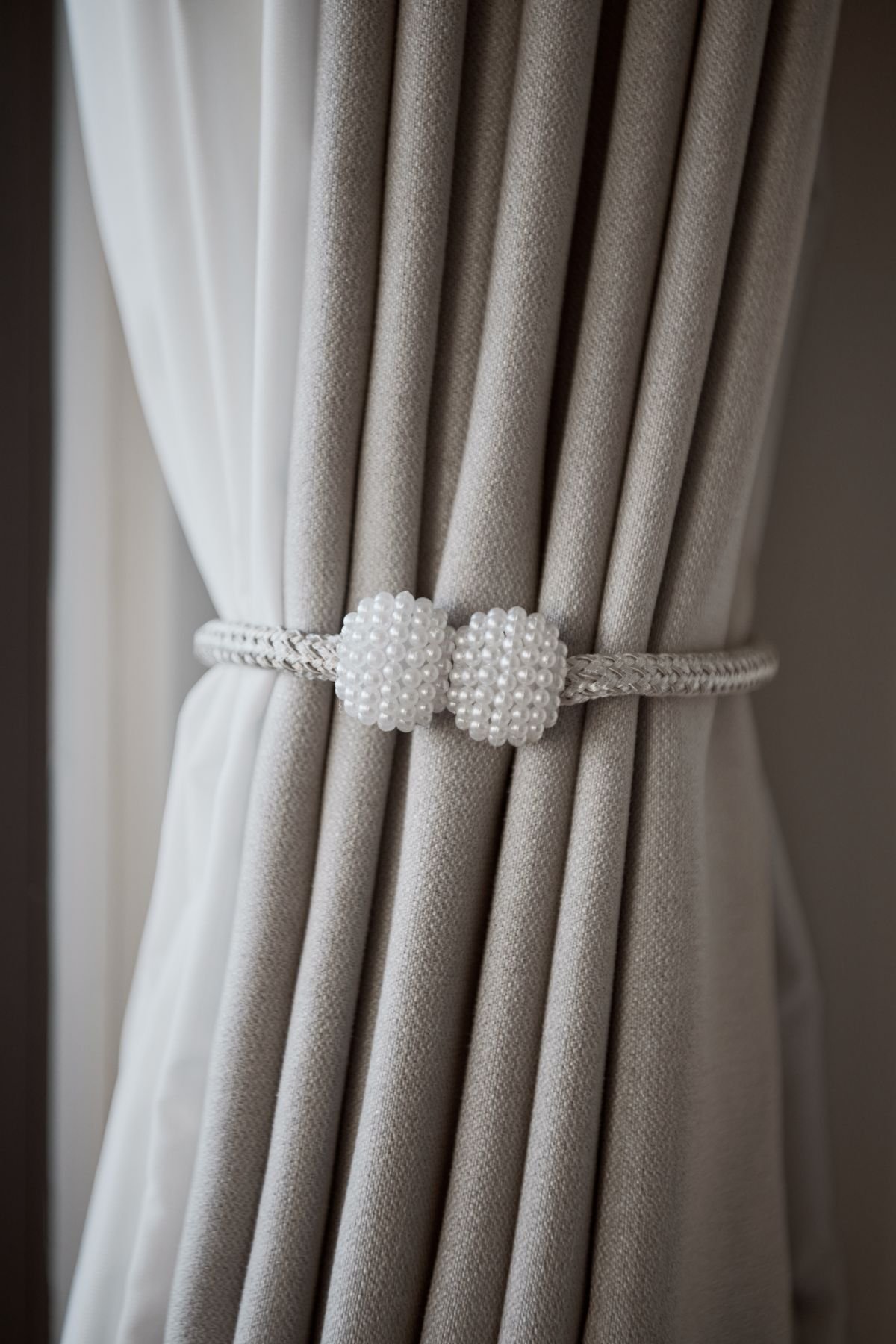 Close-up of gray pleated drapes held with a pearl-style tieback.
