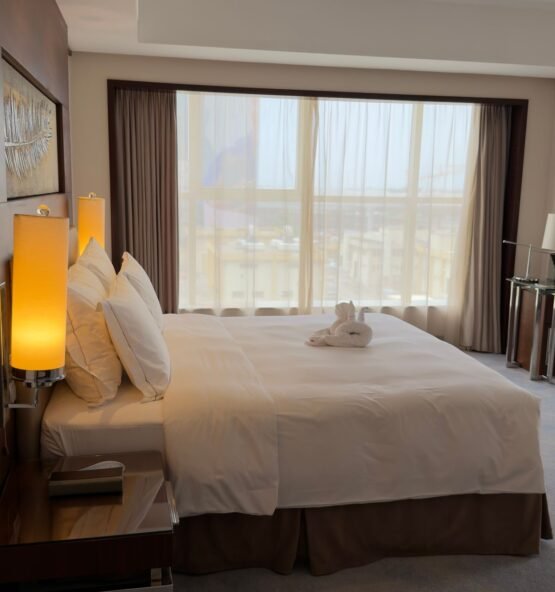 Bedroom window framed by neutral drapes in a hotel-style room.