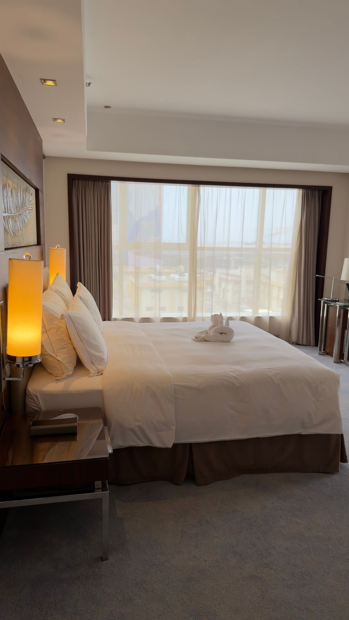 Bedroom window framed by neutral drapes in a hotel-style room.
