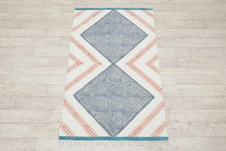 Light rug with blue diamond motifs and coral accents on a wooden floor.