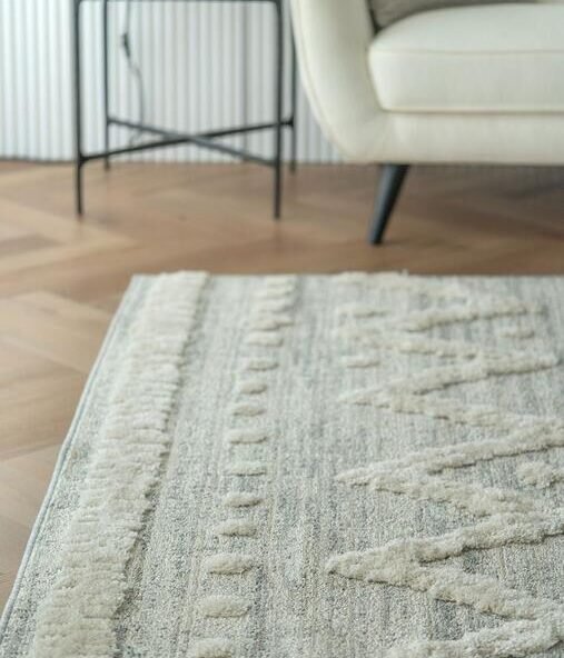 Close view of a textured ivory rug beside a chair in a bright room.