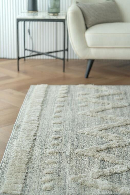 Close view of a textured ivory rug beside a chair in a bright room.